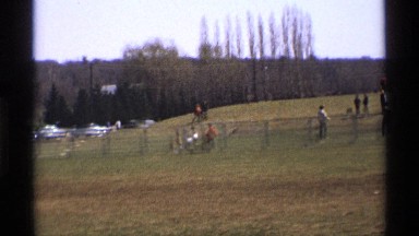 1969: peoples walking through a ground surrounded by trees where lot of cars