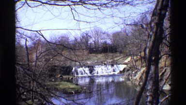 1969: closeup of small dam with a cascade in a rural setting in springtime