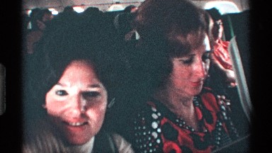 1971: two women and child seated inside an airplane.,one of them speaks to