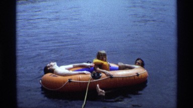1971: young girl sits in middle of inflatable float between two young men