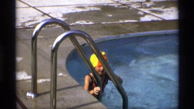 1971: a girl in an oversized swim cap climbs out of pool NEW YORK