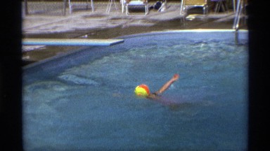 1971: a view of a swimming pool, a child swimming across. NEW YORK
