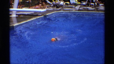 1971: a small child is swimming in the pool filled with blue water in the hot