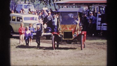 1969: a car is going over a muddy road, beside peoples are staring on the cars