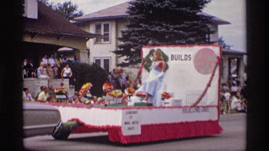 1969: people riding down the road in a parade atop floats while being pulled
