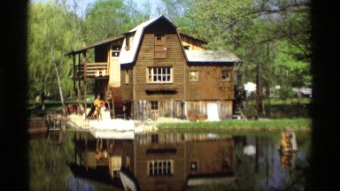 1969: old lake house with a waterwheel with a man tending to the wheel.