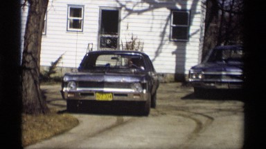 1966: a car move in the parking place another place near leafless tree and road