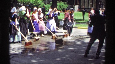 1969: women dressed in maid uniforms cleaning the street with push brooms.
