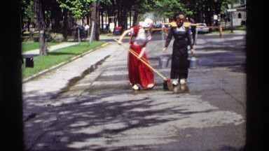 1969: old lady wearing a amish outfit, washing the streets blocking traffic.