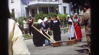 1969: a group of women in clogs, and dutch hats are sweeping water on a street