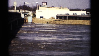 1969: rushing water in a channel goes by a sparsely populated residential area