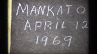 1969: a small sign placed upon a piece of a tree in a field with writing on it.