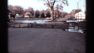 1969: slatted fencing blocks entry to residential road by a pond and puddles