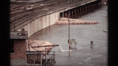 1969: water flows over the metal iron pipe connected near bridge having railway