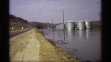 1969: commercial metal structures stand on flooded land as car passes