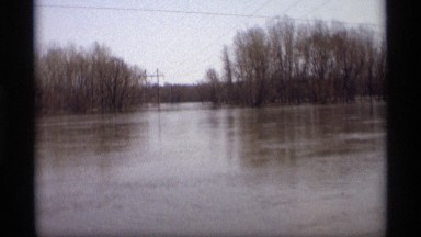 1969: road trip beside a flooded area with trees and village countryside. SAVAGE