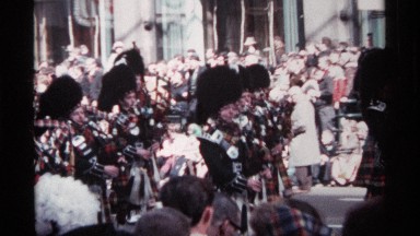 1968: scottish pipers in full regalia march in a parade in front of a crowd of