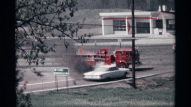 1968: firetruck stops by smoking car at intersection while traffic passes