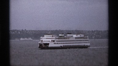 1974: a ferry slowly navigates peaceful waters in front of a sprawling urban