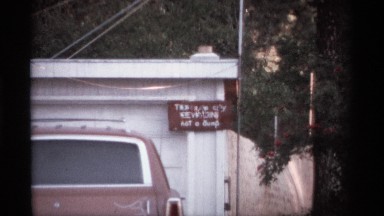 1974: a small house with a name board and a car parking at front some plants