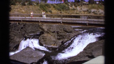 1974: long bridge with side water fall,two people viewing the scene, WORLDS FAIR