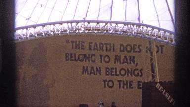 1974: sign painted on wall stating "earth does not belong to man, man belongs to