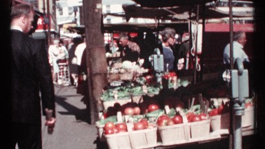 1967: man dressed in suit walking through open market, looking at fresh produce