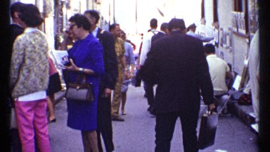 1967: Man Adjusts Jacket While Walking Through Busy Market of Tourists and Artists