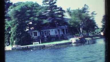 1967: large house by waterfront is partly hidden and framed by tall trees