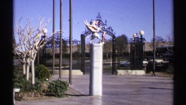 1972: an iron gate entrance is flanked by poles and a column with a sculpture