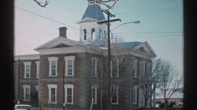 1972: large structure standing in town with a few people walking around outside