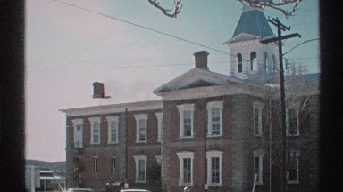 1972: a large building with roof top and some cars are parking there and it