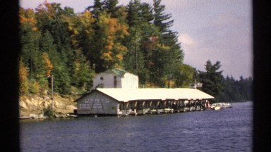 1971: view of a lakeside port structure on a sunny day as a boat is docked NEW