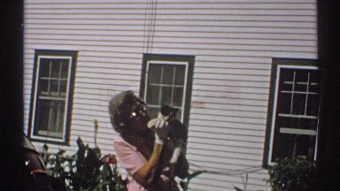 1971: old grandma talking to black and white cat while standing in front of a