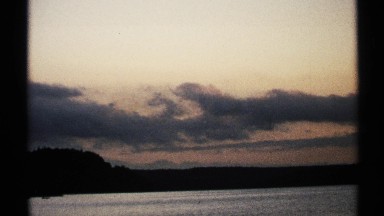 1971: dark clouds hang over darker contoured land bordering body of water NEW