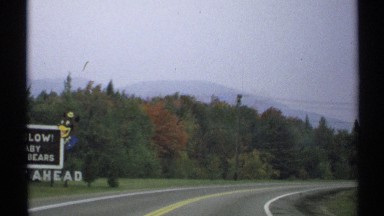 1971: a person in a car driving on the road passing a sign. NEW YORK