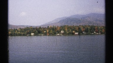 1971: homes line the forested shore of a lake sitting at the foot of mountains