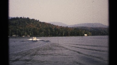 1971: a boat sails in the sea that is next to the hills covered with trees. NEW