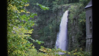 1971: rushing waterfall on the side of a cliff, next to an old building