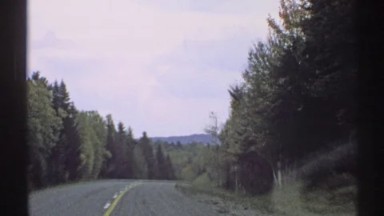 1971: view from a moving vehicle traveling down a highway lined with forest