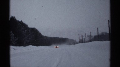 1971: a car travels on a road covered with snow in a cloudy day. WISCONSIN