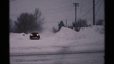 1971: snow area with trees,electric wire is present and a car is moving on the