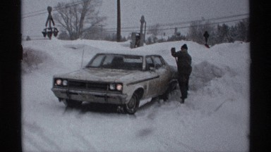1971: man digs out car surrounded with snow using small-blade garden shovel