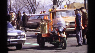 1971: emergency personnel gathering in stopped traffic and an official getting