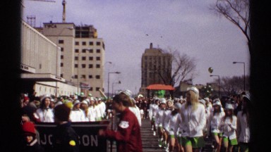 1971: many men and women are marching in a parade outside with buildings in the