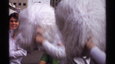 1971: a parade including cheerleaders and a float march through a crowd