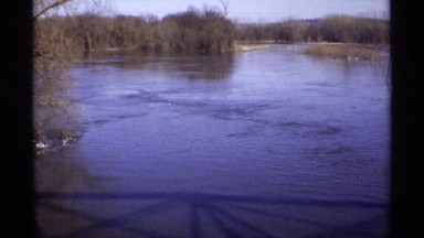 1971: shadow of railing falls over water flowing away toward land and trees