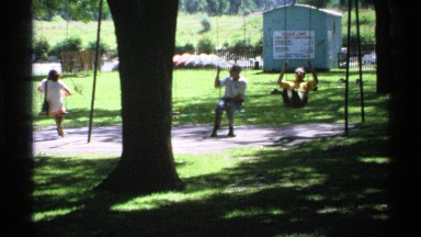 1970: two boys and a girl on swings at a playground in the summer in the daytime