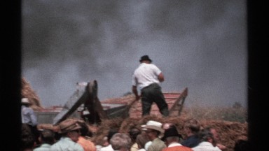 1971: thick black smoke blows across the background as a worker tosses hay from