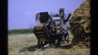 1971: farm thresher stands idle next to tall pile of inedible plant material